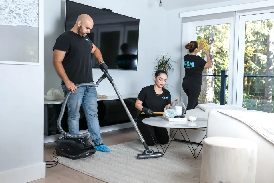 Two C&M cleaners vacuuming and dusting a Vancouver living room